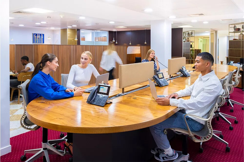 Client working and answering calls at Mayfair Coworking Space featuring a high shared desk and booths.